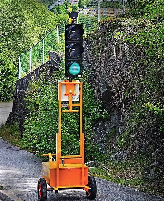 Mobilt trafikklys montert på en gul tralle, plassert langs en vei.