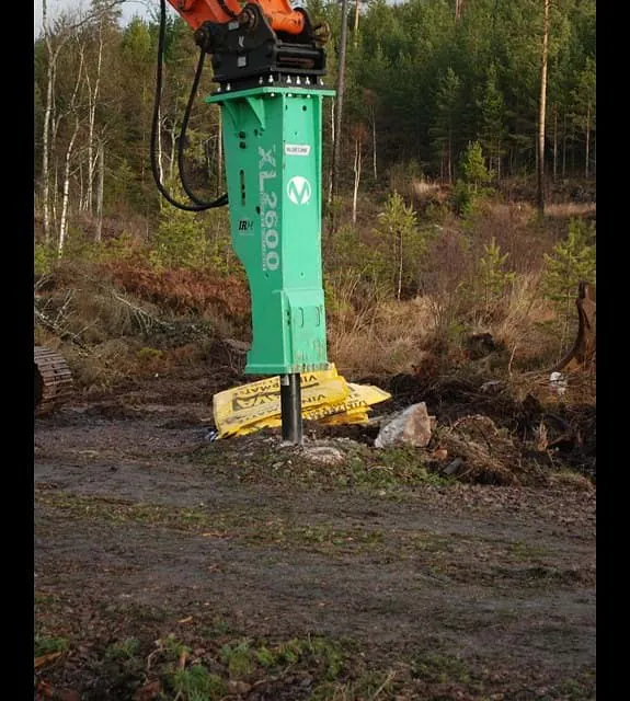 Hydraulisk hammer montert på gravemaskinarm i arbeid på en byggeplass.