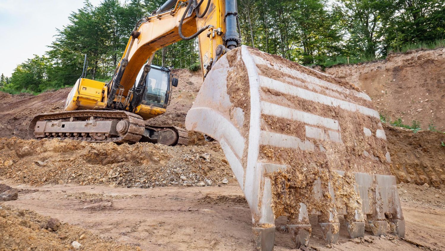 En stor gul gravemaskin graver i en jordvoll på en byggeplass.