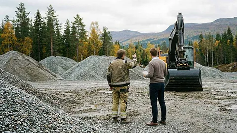 To personer ser på gravemaskin på anleggsområde